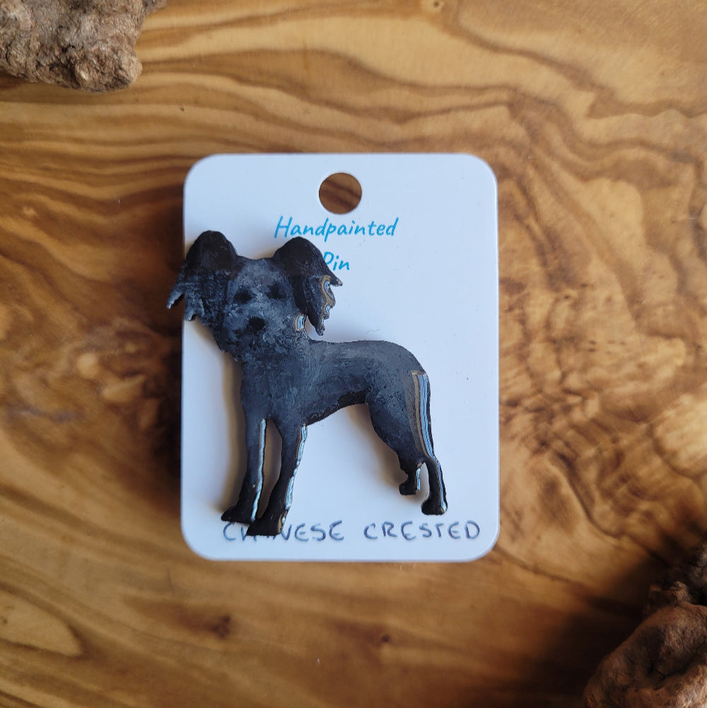 Handpainted Chinese Crested dog pin on a wooden surface