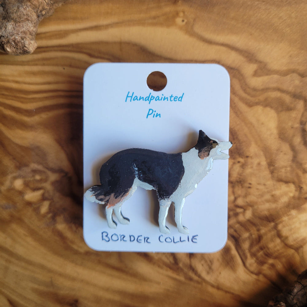 Handpainted pin of a border collie on a white card with text, placed on a wooden surface.