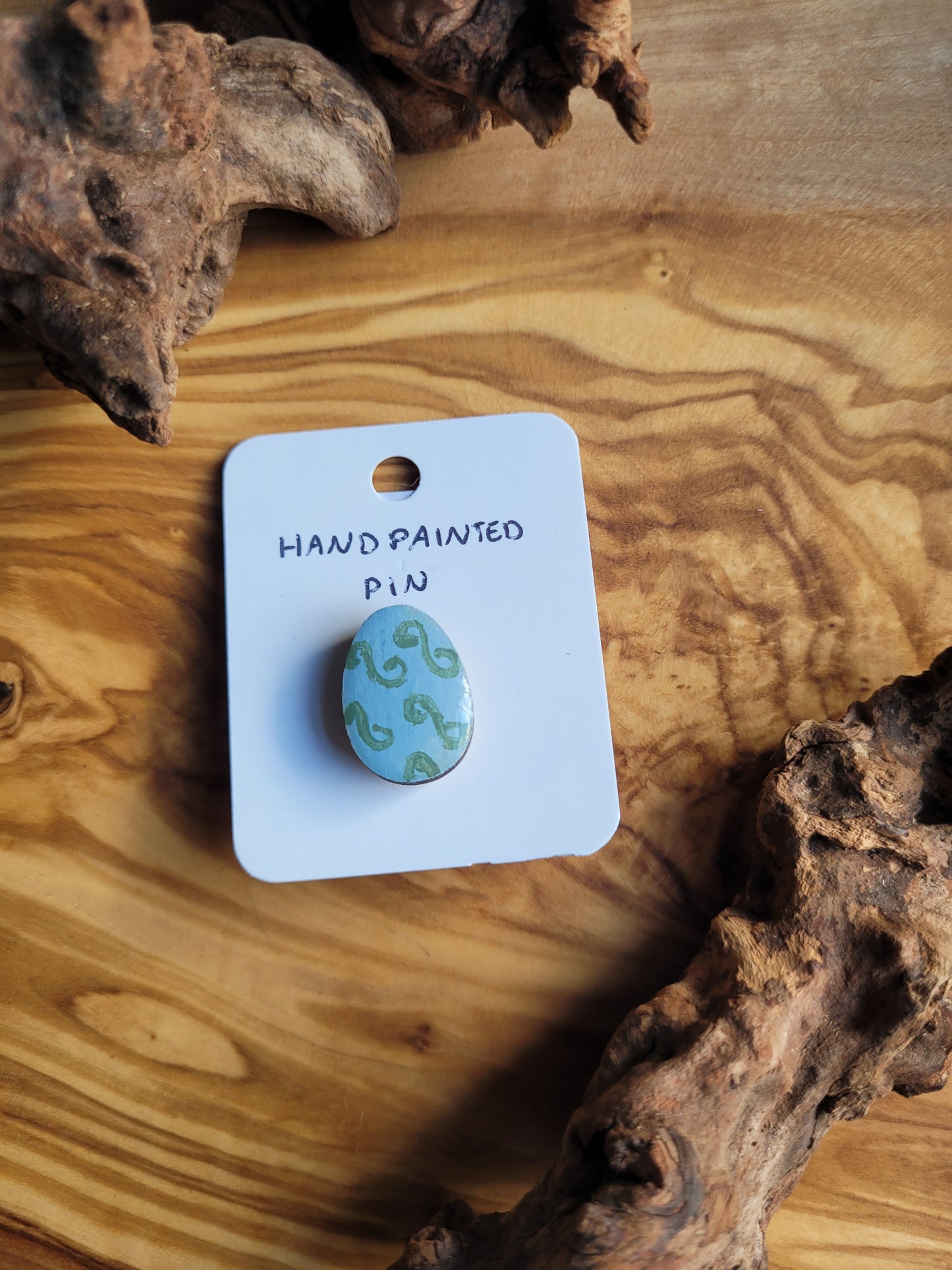 Hand-painted wooden Easter Egg shaped pin badge with green swirls on a blue background