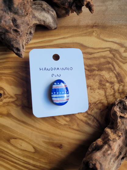 Hand-painted wooden Easter Egg shaped pin badge with blue, white and red patterns painted across a blue egg