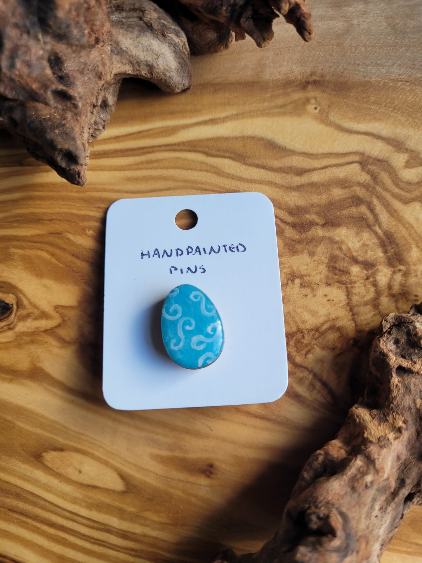 Hand-painted wooden Easter Egg shaped pin badge with light blue swirls on a tad darker blue background