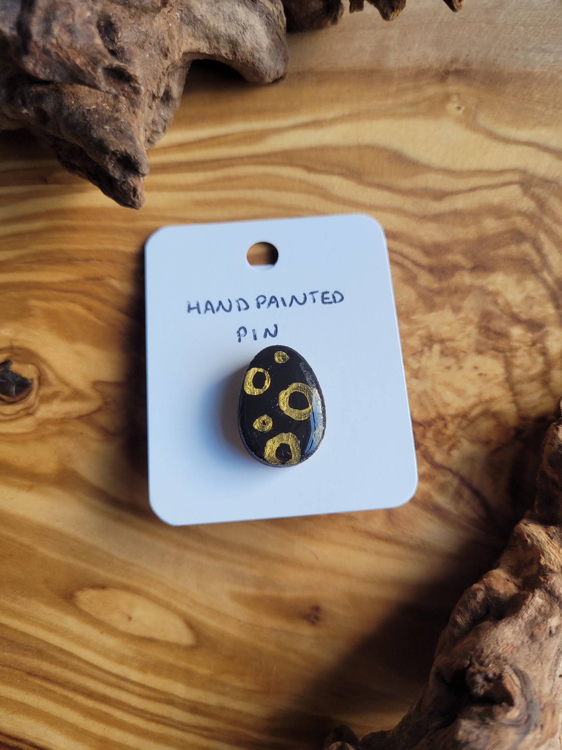 Hand-painted wooden Easter Egg shaped pin badge with gold circles on a black background
