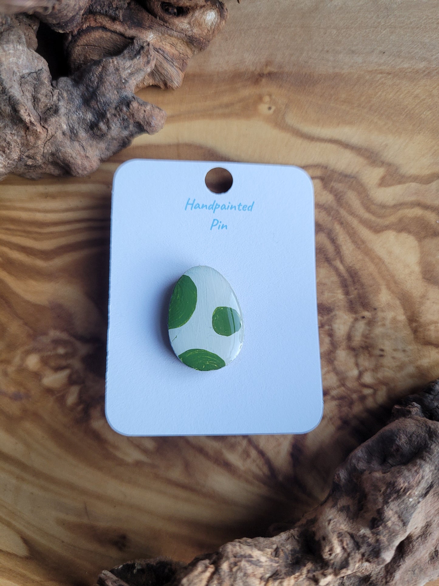 Hand-painted wooden Easter Egg shaped pin badge with green patches on a white egg 