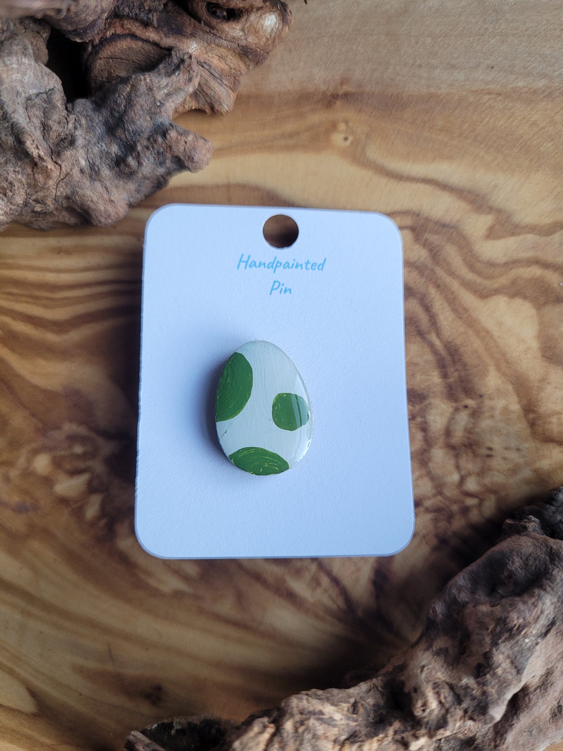 Hand-painted wooden Easter Egg shaped pin badge with green patches on a white egg 