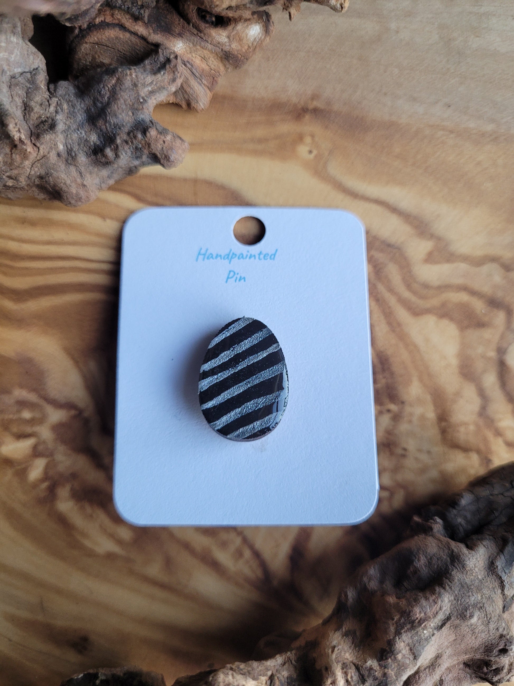 Hand-painted wooden Easter Egg shaped pin badge with silver stripes on a dark background