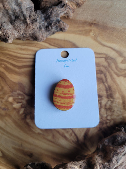 Hand-painted wooden Easter Egg shaped pin badge with orange patterns painted over a deep yellow background
