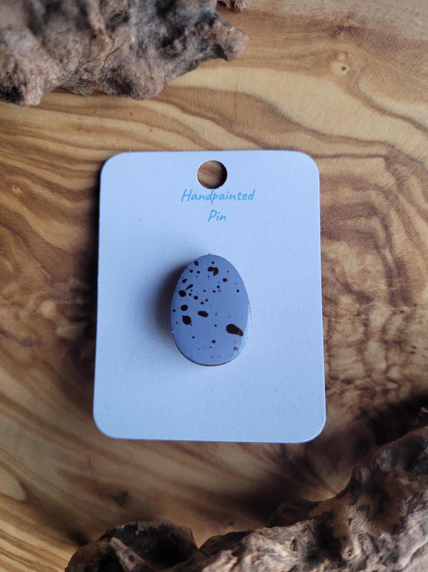 Hand-painted wooden Easter Egg shaped pin badge with dark speckles on a lilacy blue egg like a chocolate mini egg