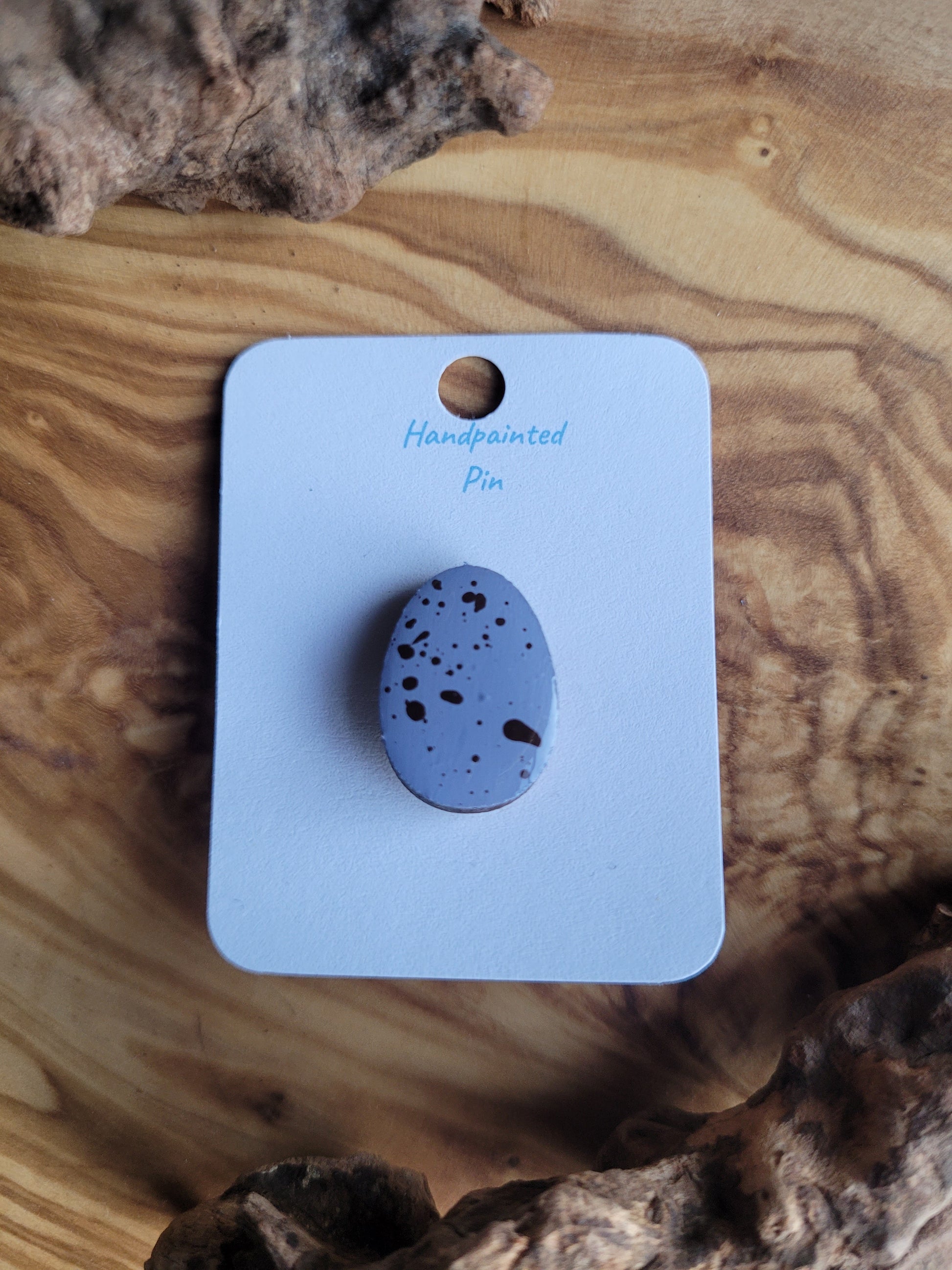Hand-painted wooden Easter Egg shaped pin badge with dark speckles on a lilacy blue egg like a chocolate mini egg