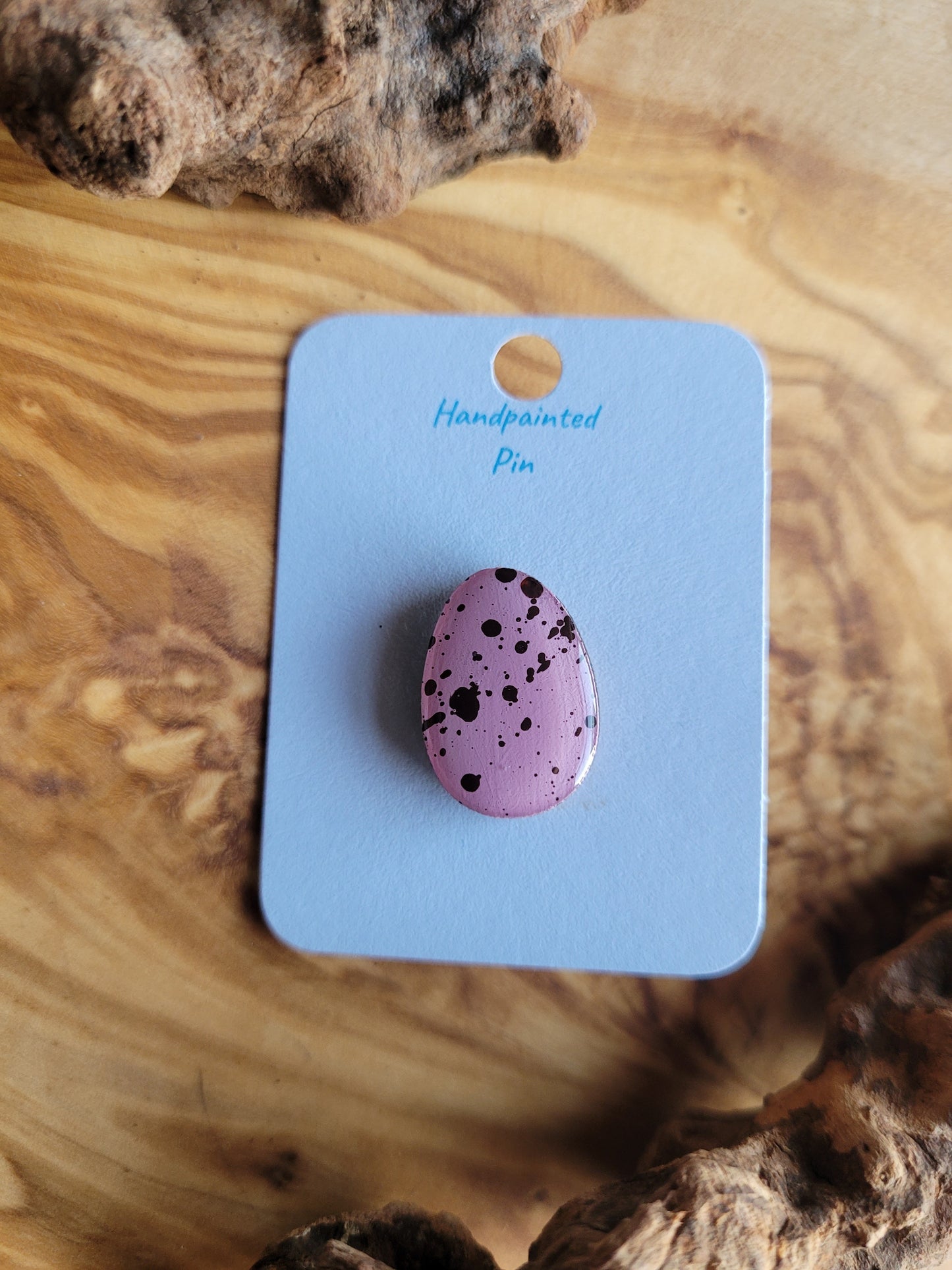 Hand-painted wooden Easter Egg shaped pin badge with dark speckles on a pink background egg