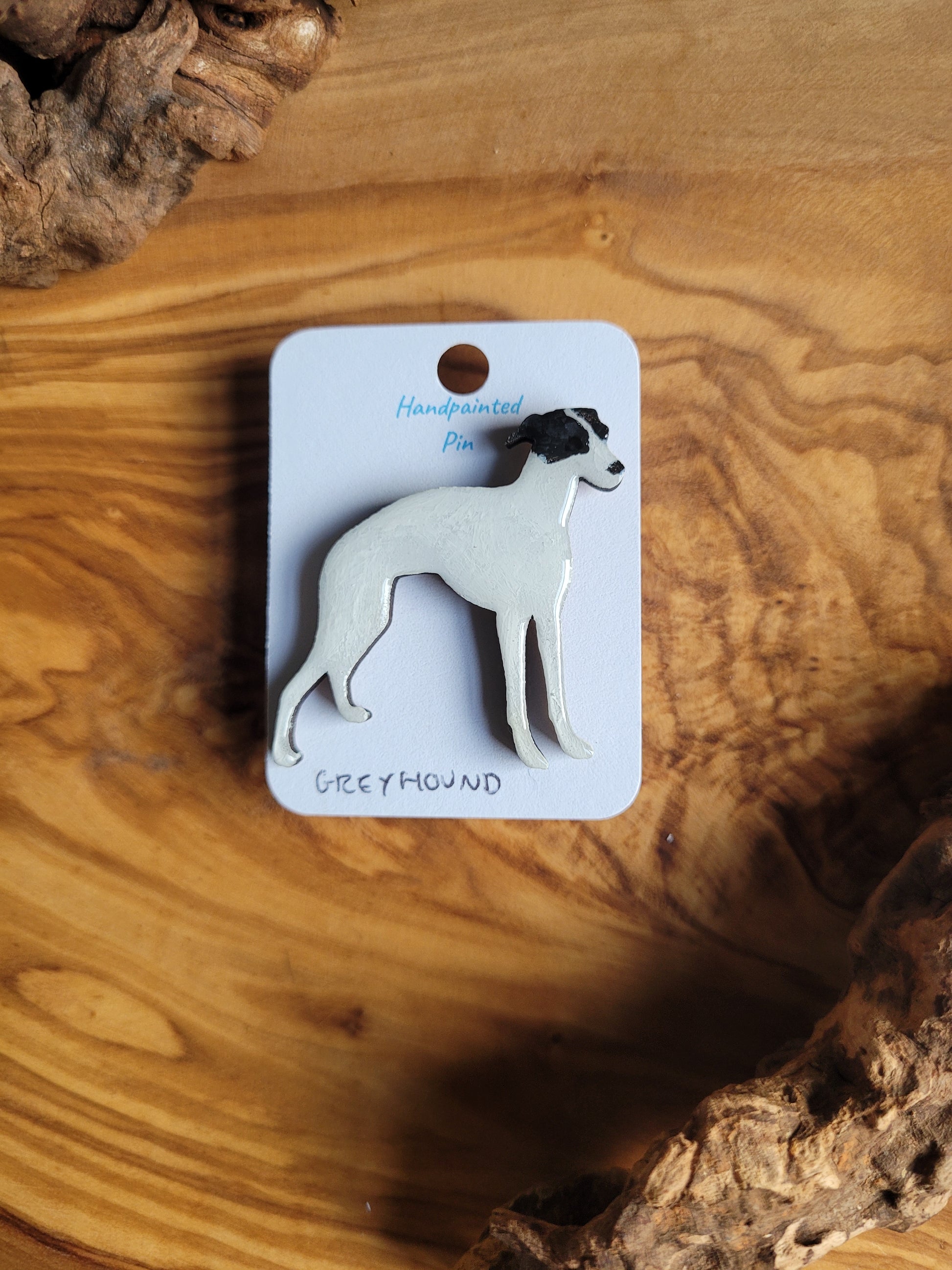 Hand-painted Greyhound pin badge, painted onto wood. White with black patches over eyes and ears