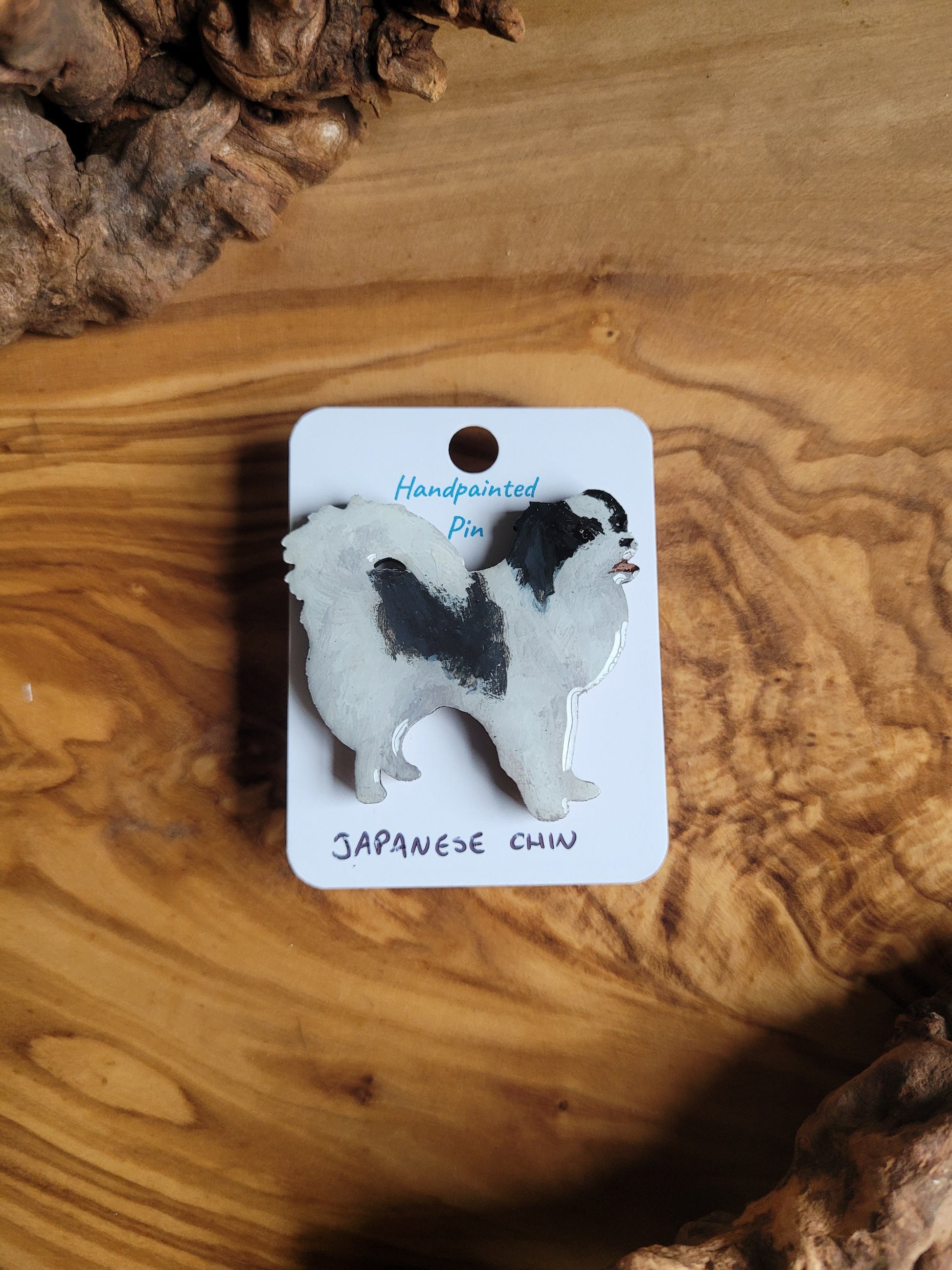 Black and white coloured, hand-painted, wooden pin badge of a Japanese Chin dog