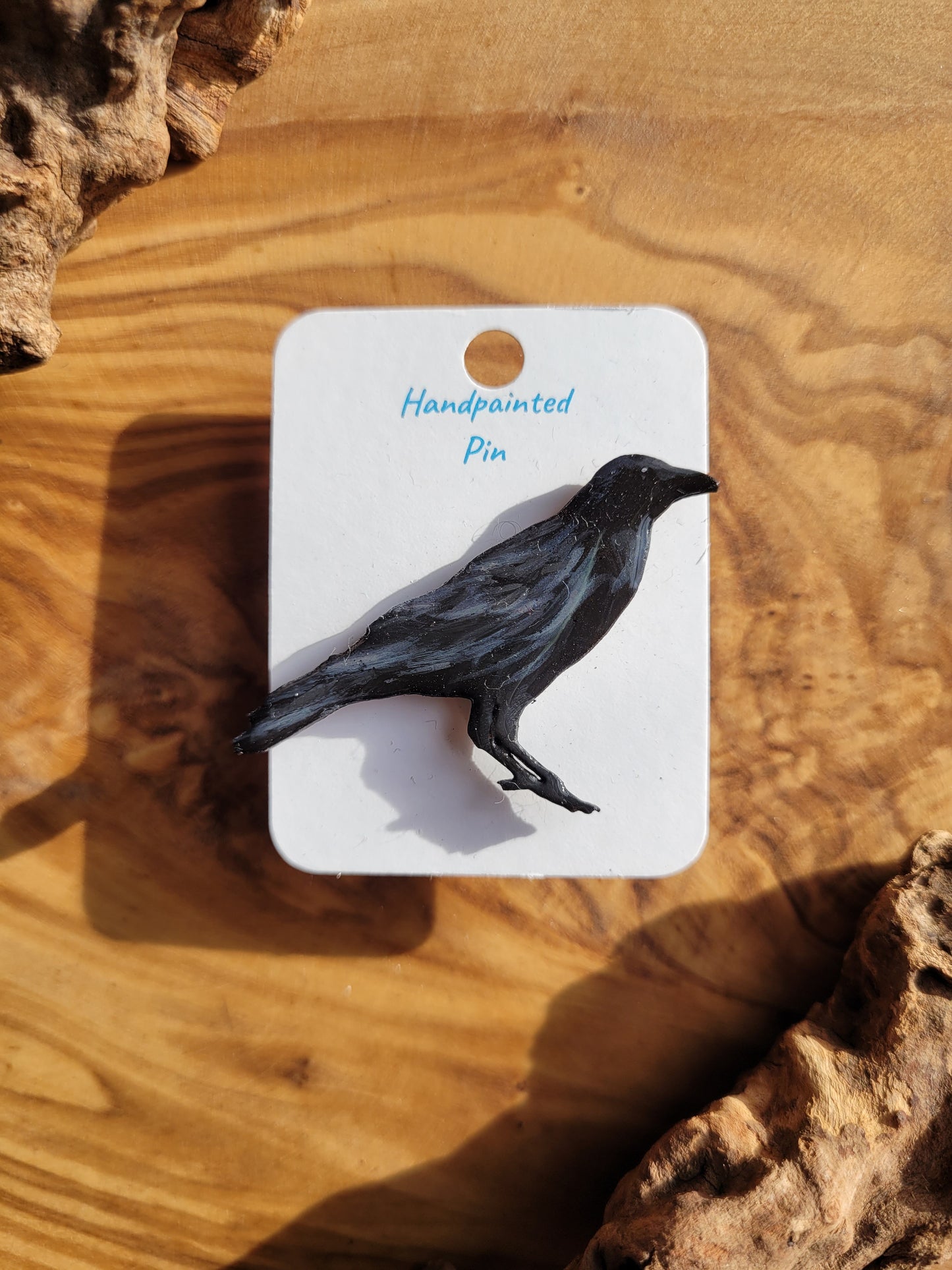 Hand-painted wooden pin badge of a perched black raven