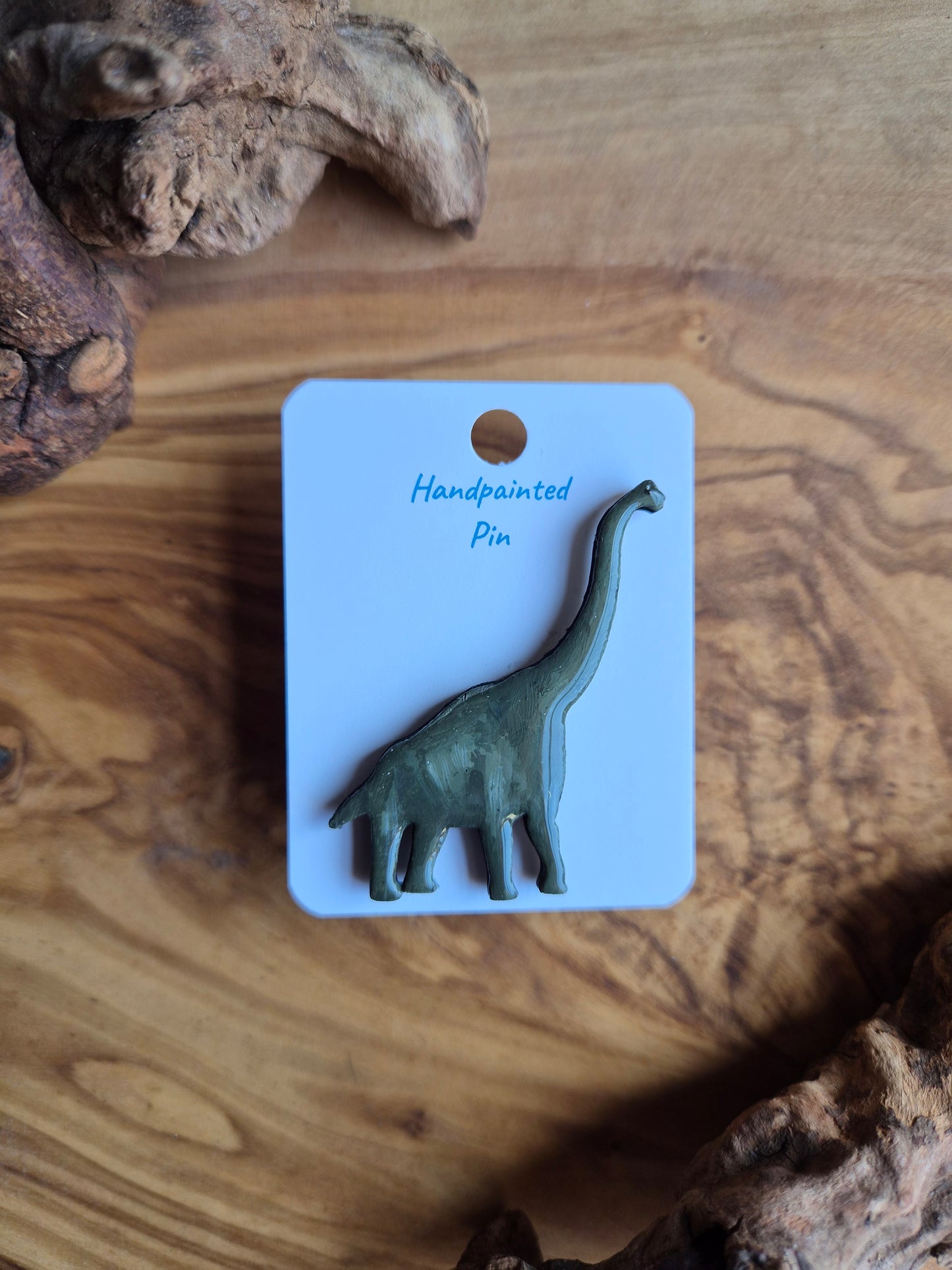 A hand-painted wooden dinosaur pin badge of the giant giraffatitan dinosaur