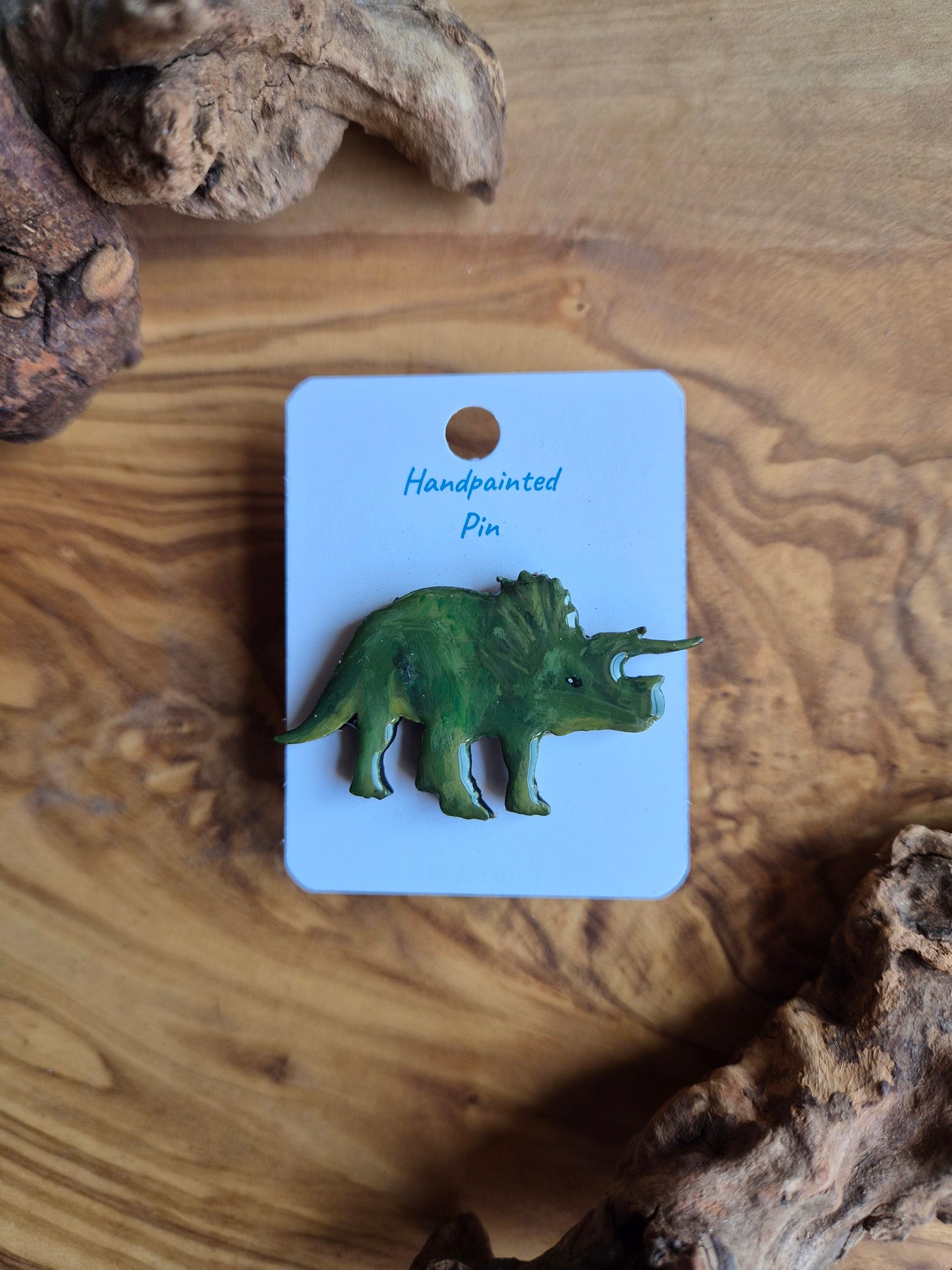A hand-painted wooden dinosaur pin badge of the iconic triceratops dinosaur