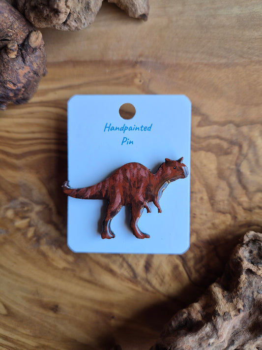 A hand-painted wooden dinosaur pin badge of a red carnotaurus dinosaur