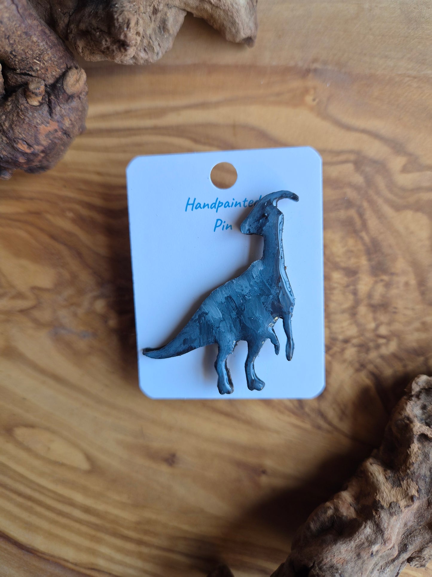 A hand-painted wooden dinosaur pin badge of the parasaurolophus dinosaur