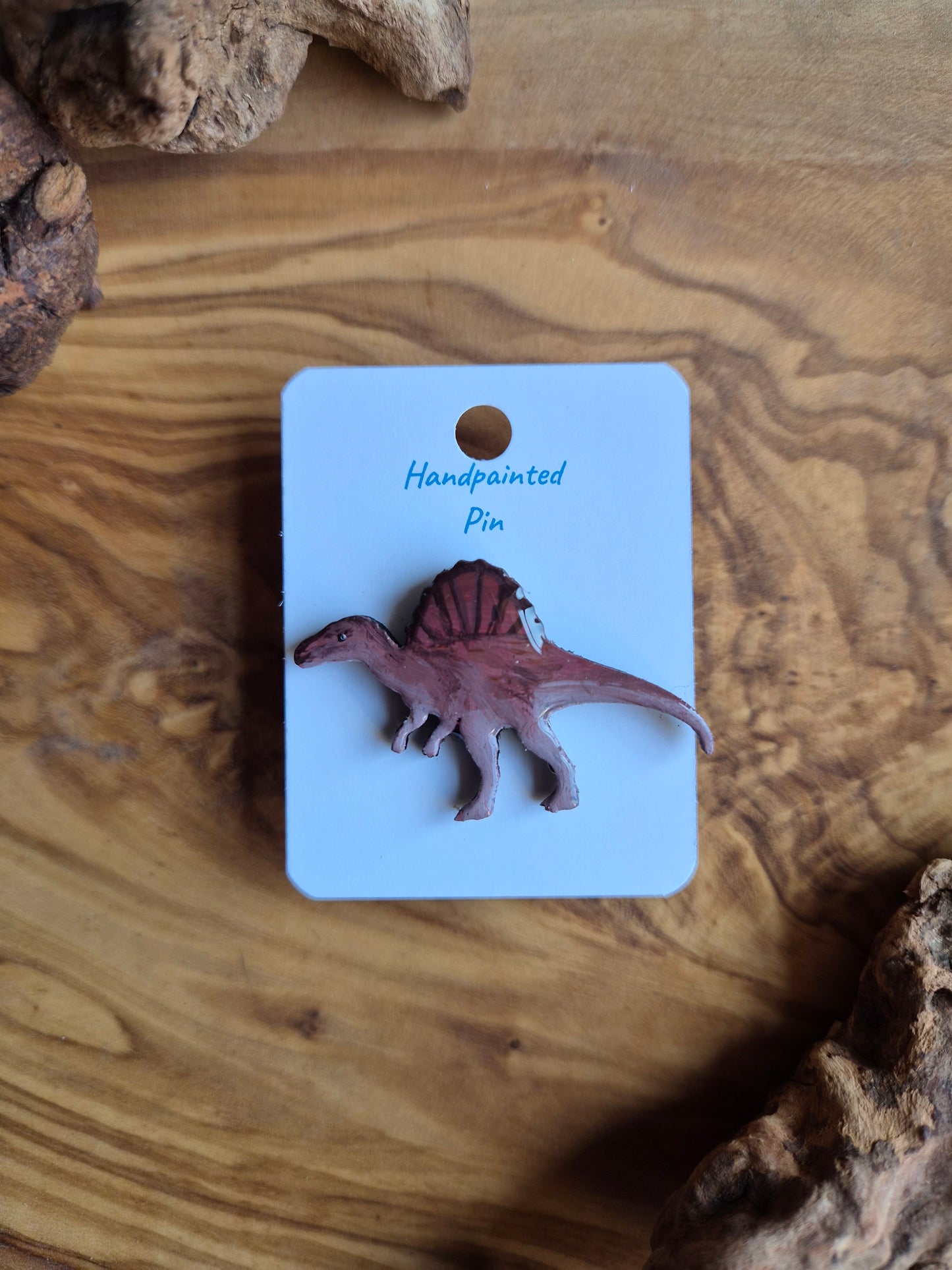 A hand-painted wooden dinosaur pin badge of the spinosaurus dinosaur