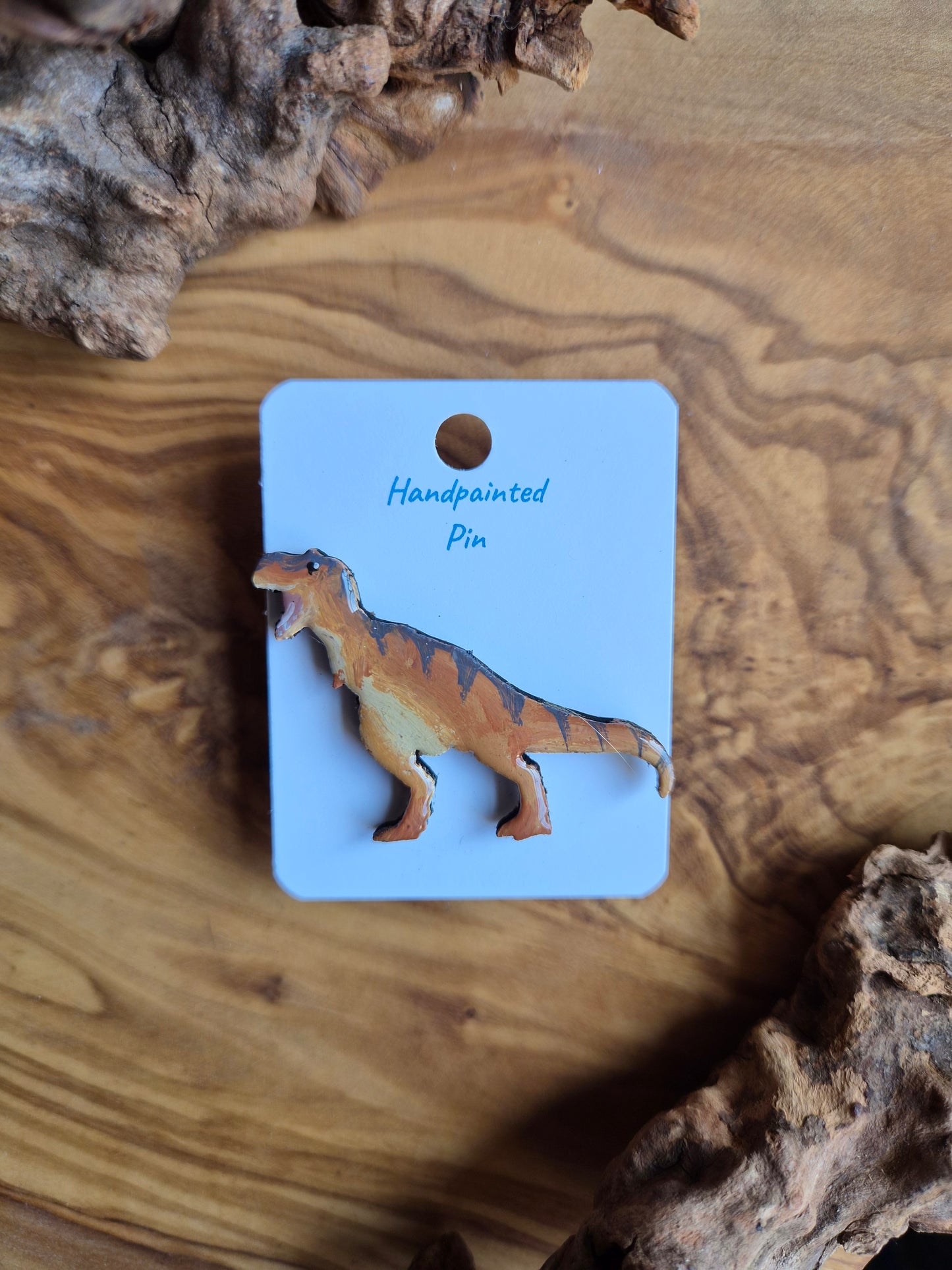 A hand-painted wooden dinosaur pin badge of the giant allosaurus dinosaur