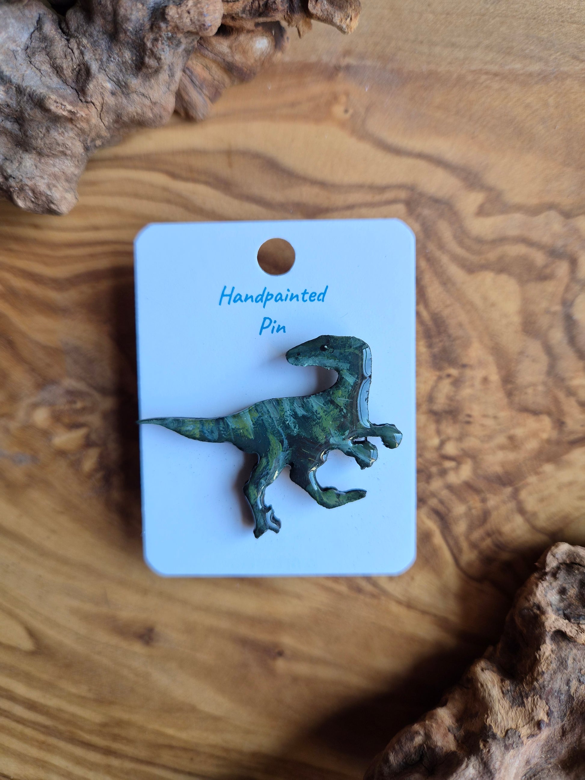 A hand-painted wooden dinosaur pin badge of the raptor dinosaur