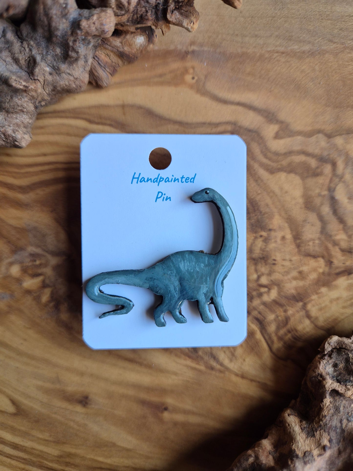A hand-painted wooden dinosaur pin badge of the fun diplodocus dinosaur