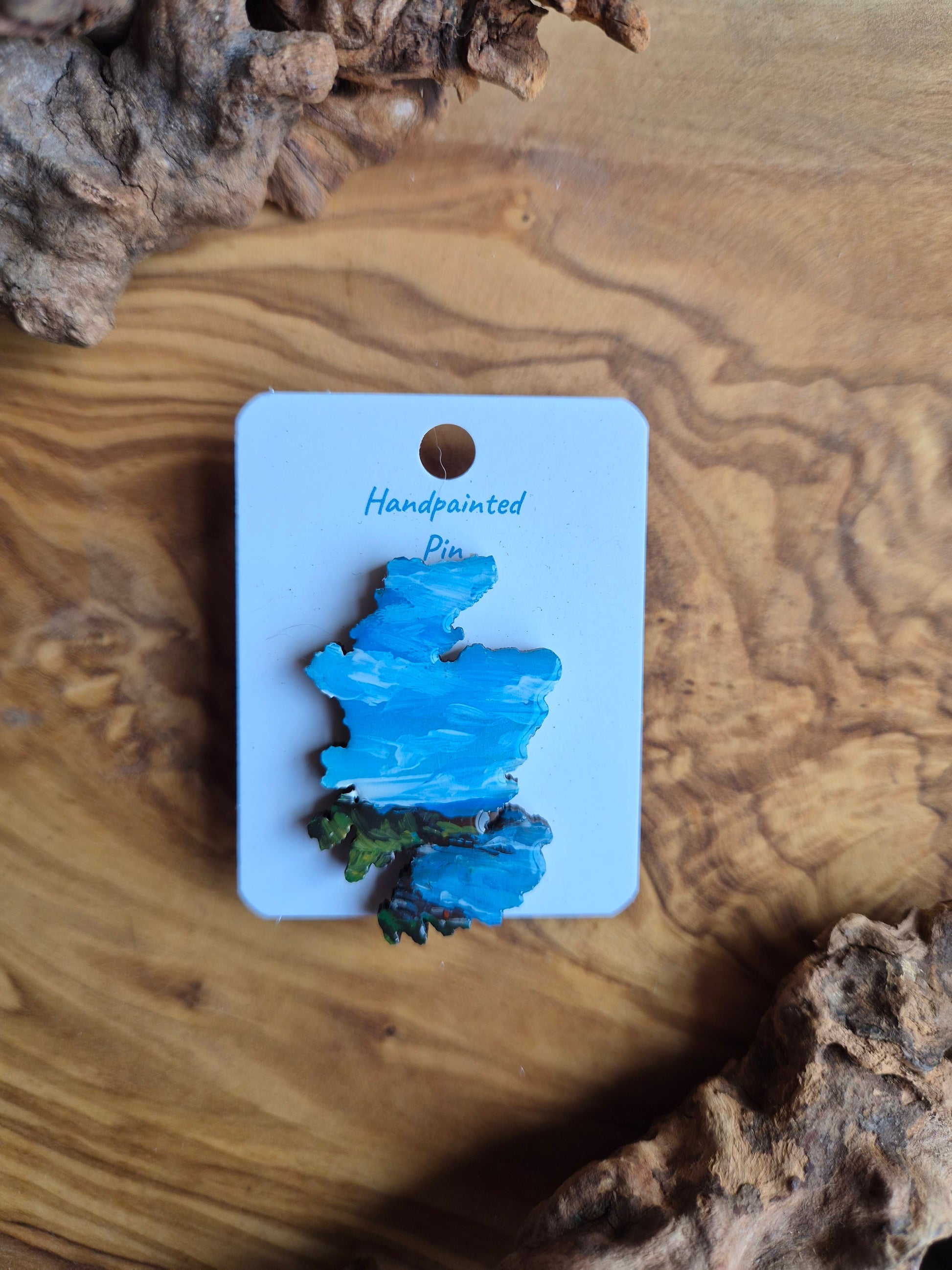 Hand-painted Scotland shaped wooden pin badge with a scottish landscape of coastal cliffs painted on