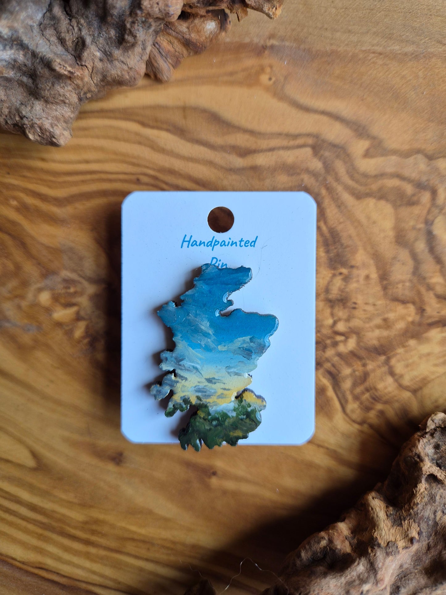 Hand-painted Scotland shaped wooden pin badge with a scottish landscape of a glowing sunset painted on