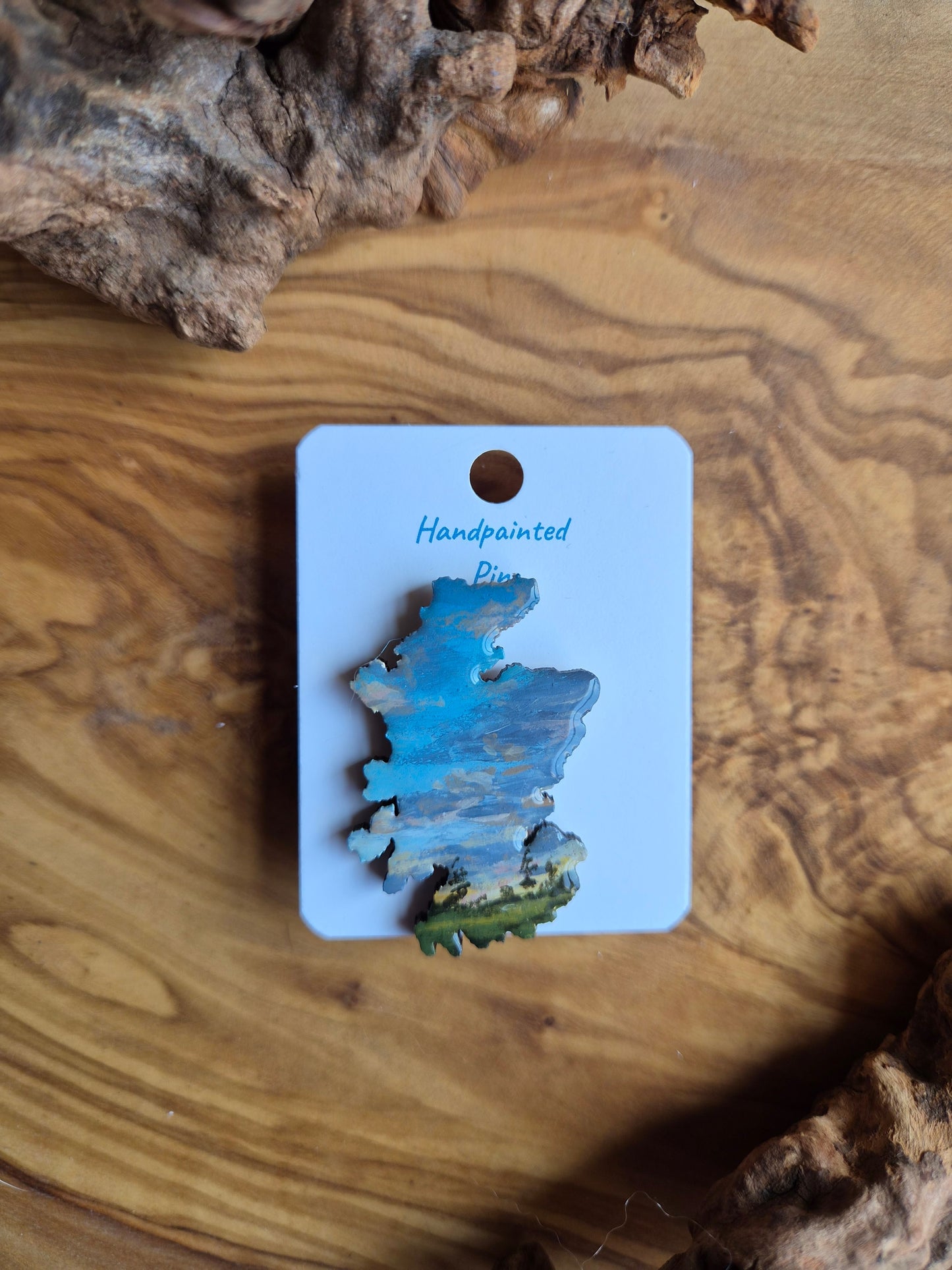 Hand-painted Scotland shaped wooden pin badge with a scottish landscape of a lilac clouded sunset painted on