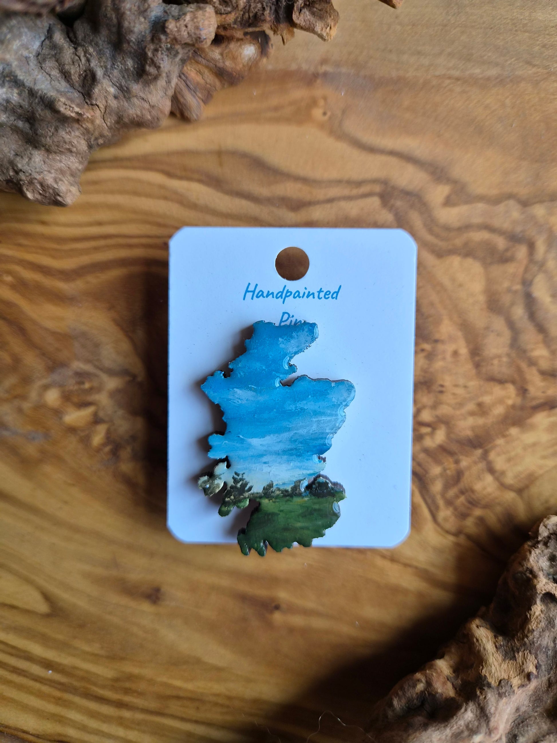 Hand-painted Scotland shaped wooden pin badge with a scottish landscape of a green park with trees painted on