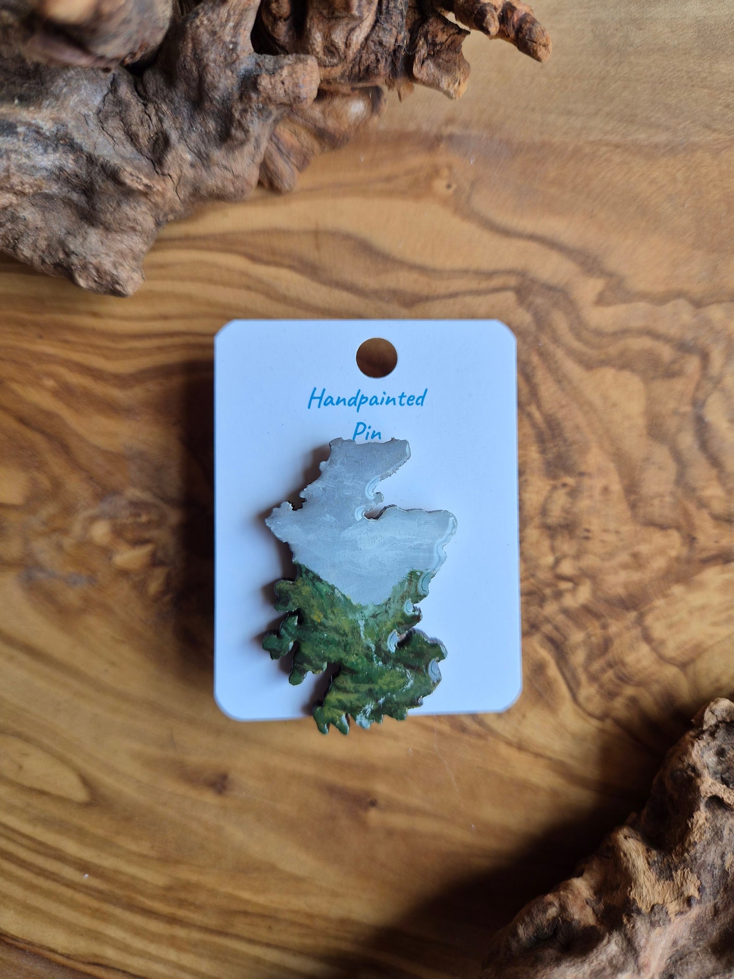 Hand-painted Scotland shaped wooden pin badge with a scottish landscape of a misty mountain with a stream painted on