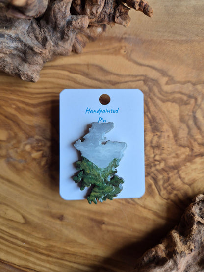 Hand-painted Scotland shaped wooden pin badge with a scottish landscape of a misty mountain with a stream painted on