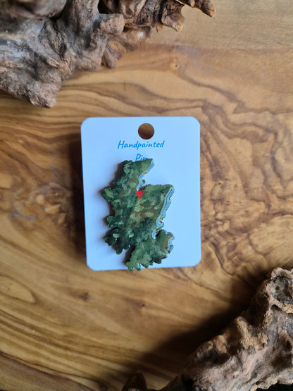 Hand-painted Scotland shaped wooden pin badge with a scottish terrain painted on with a location marker on Inverness