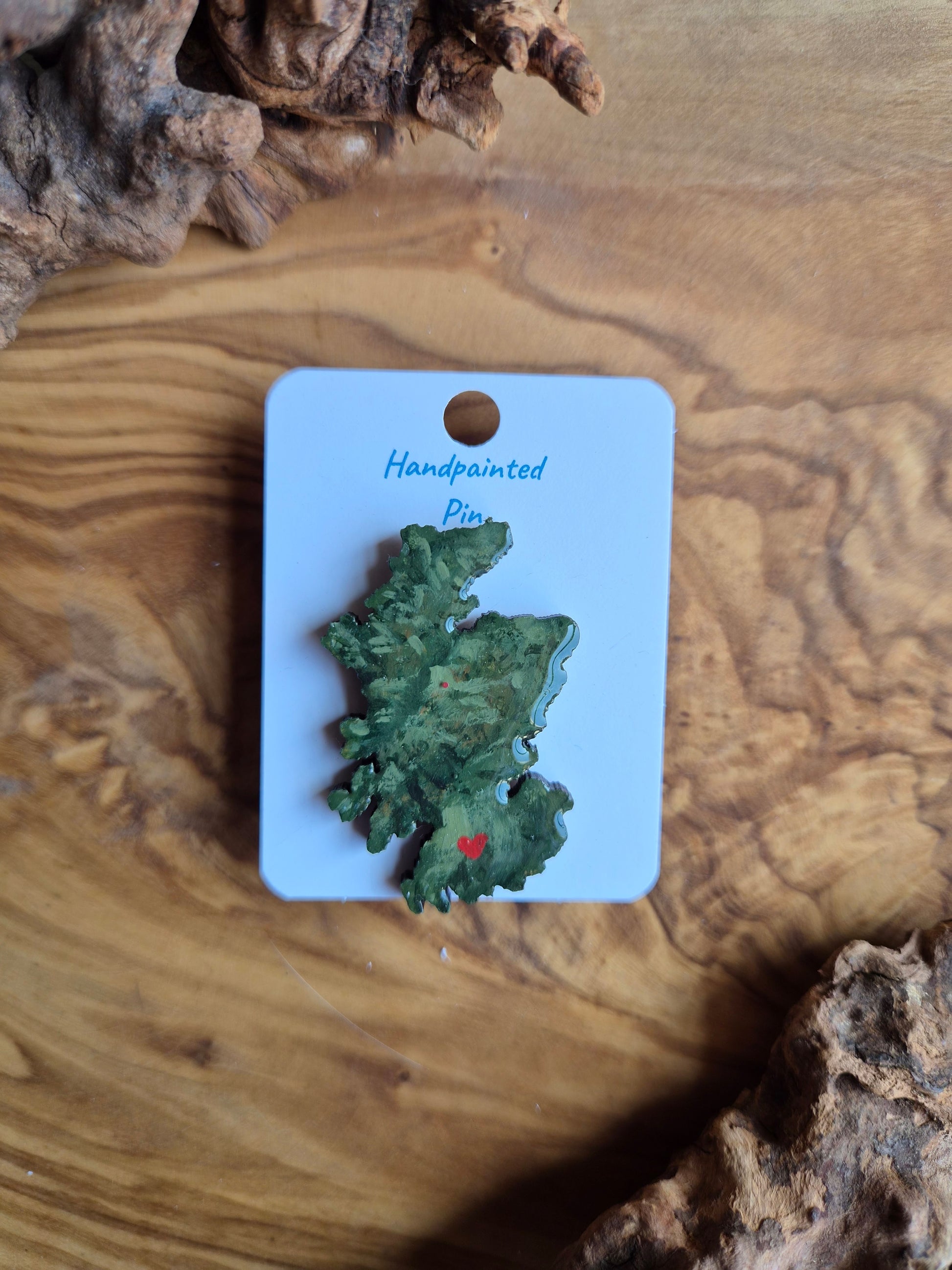 Hand-painted Scotland shaped wooden pin badge with a scottish terrain painted on with a location marker on Glasgow