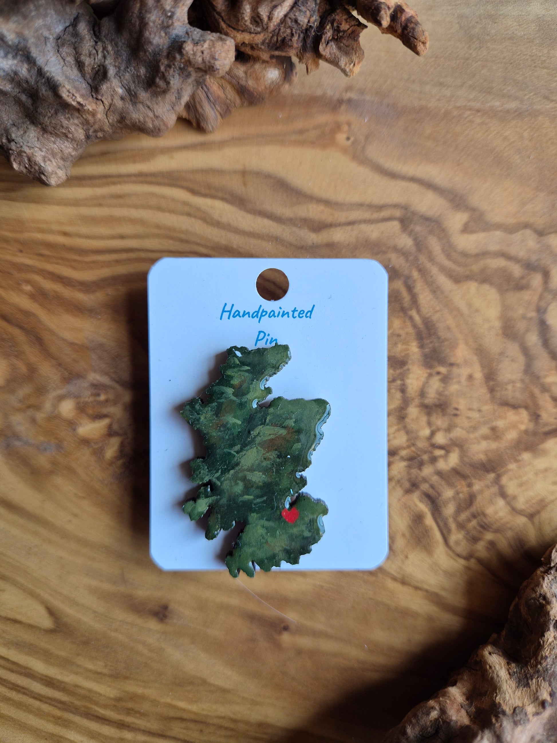 Hand-painted Scotland shaped wooden pin badge with a scottish terrain painted on with a location marker on Edinburgh