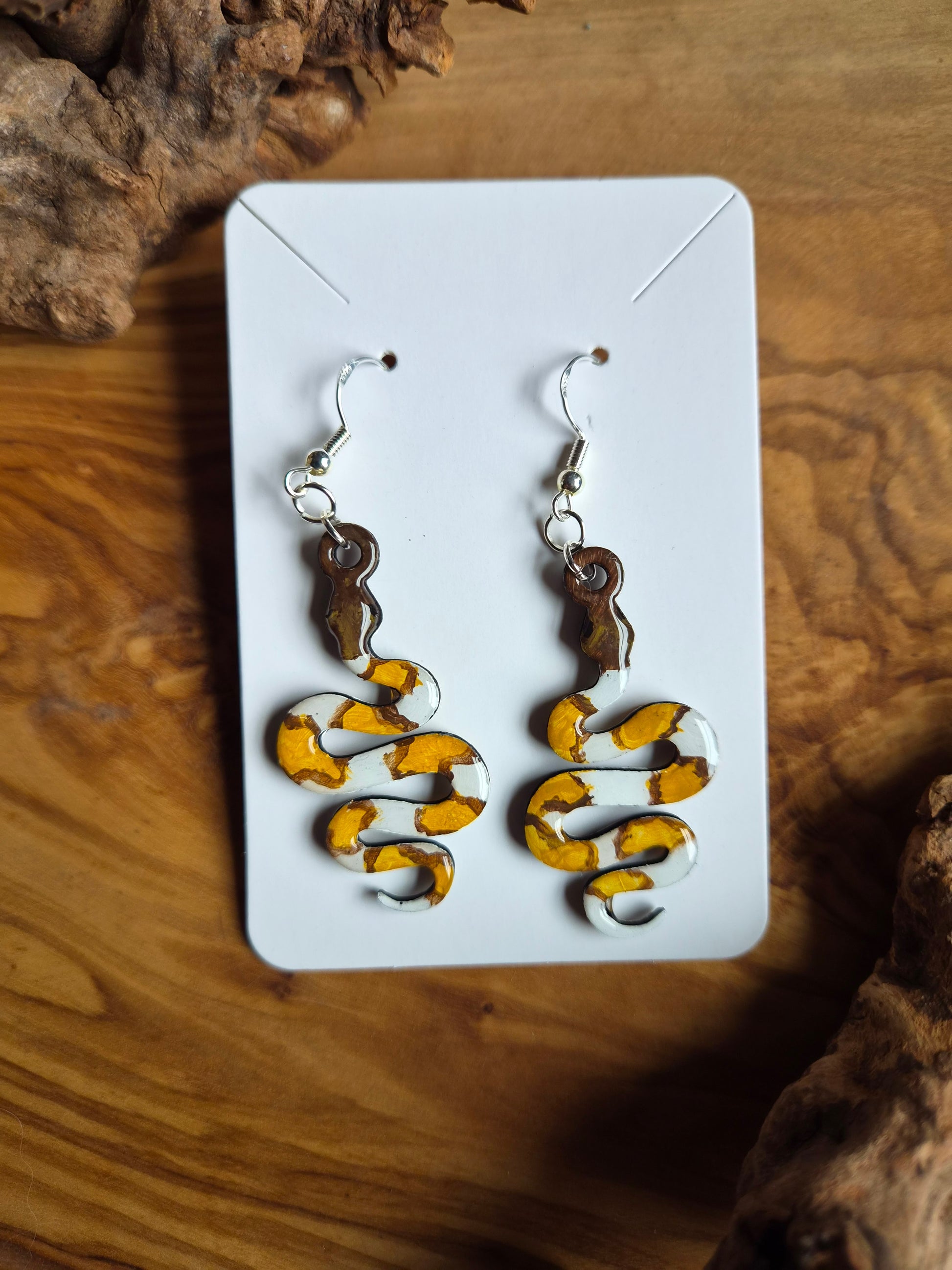 hand painted Snake-shaped wooden dangle earrings of a banana morph ball python snake on a white card with a wooden background