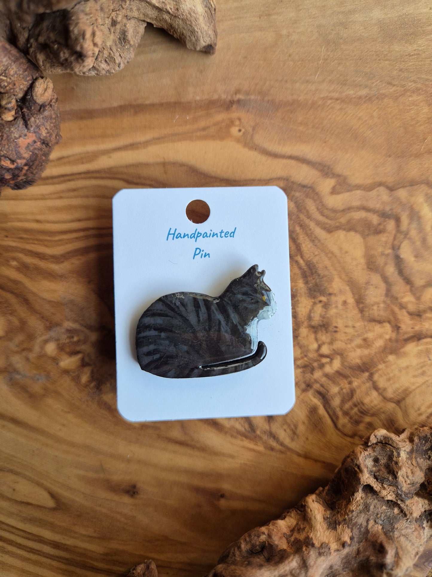 Hand-painted wooden pin badge of a dark tabby coloured cat with white