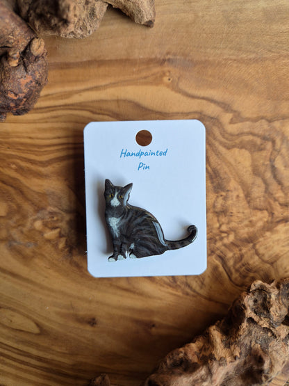 Hand-painted wooden pin badge of a dark tabby coloured cat with white face, chest and paws