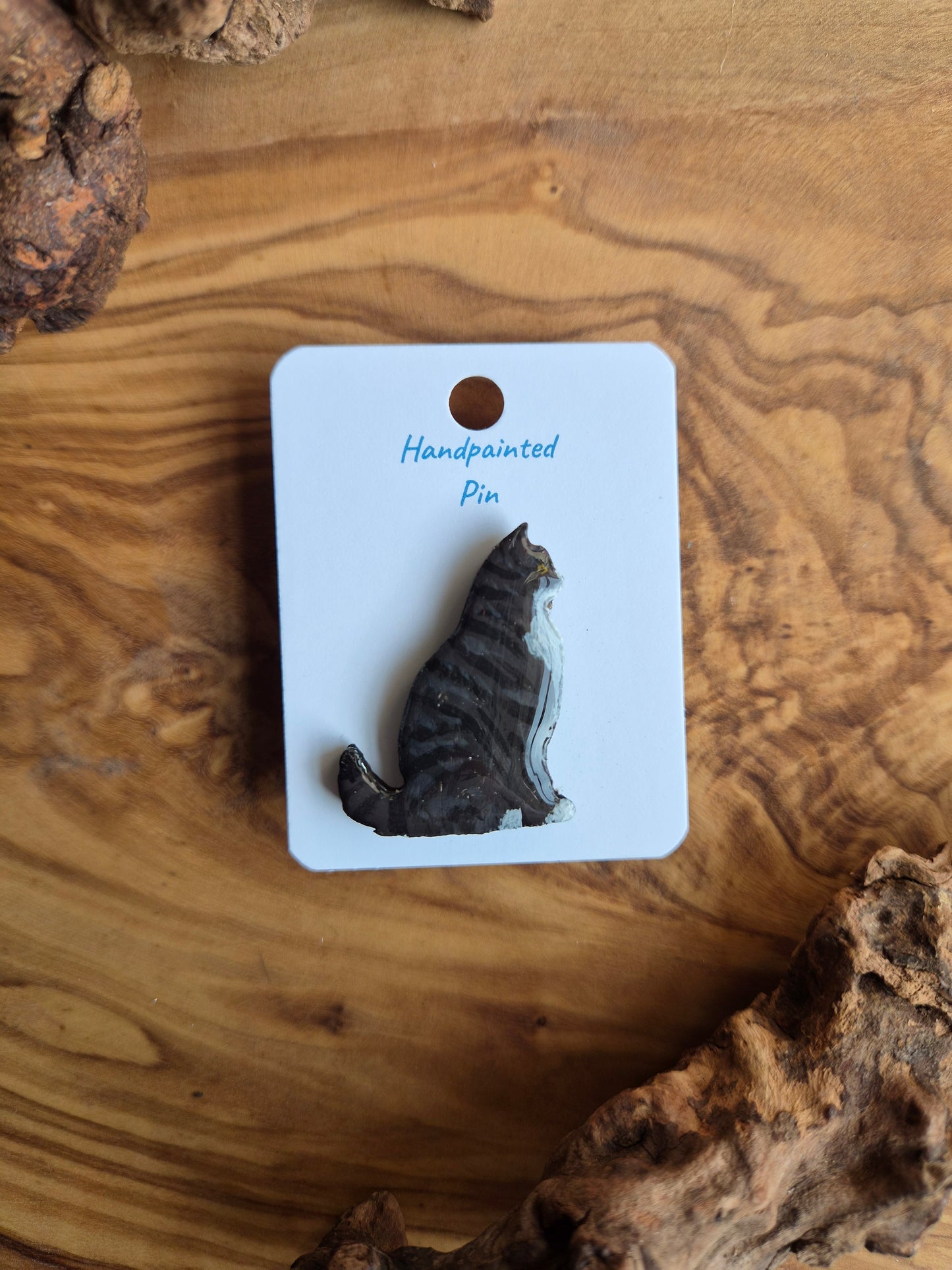 Hand-painted wooden pin badge of a dark tabby coloured cat with white chin