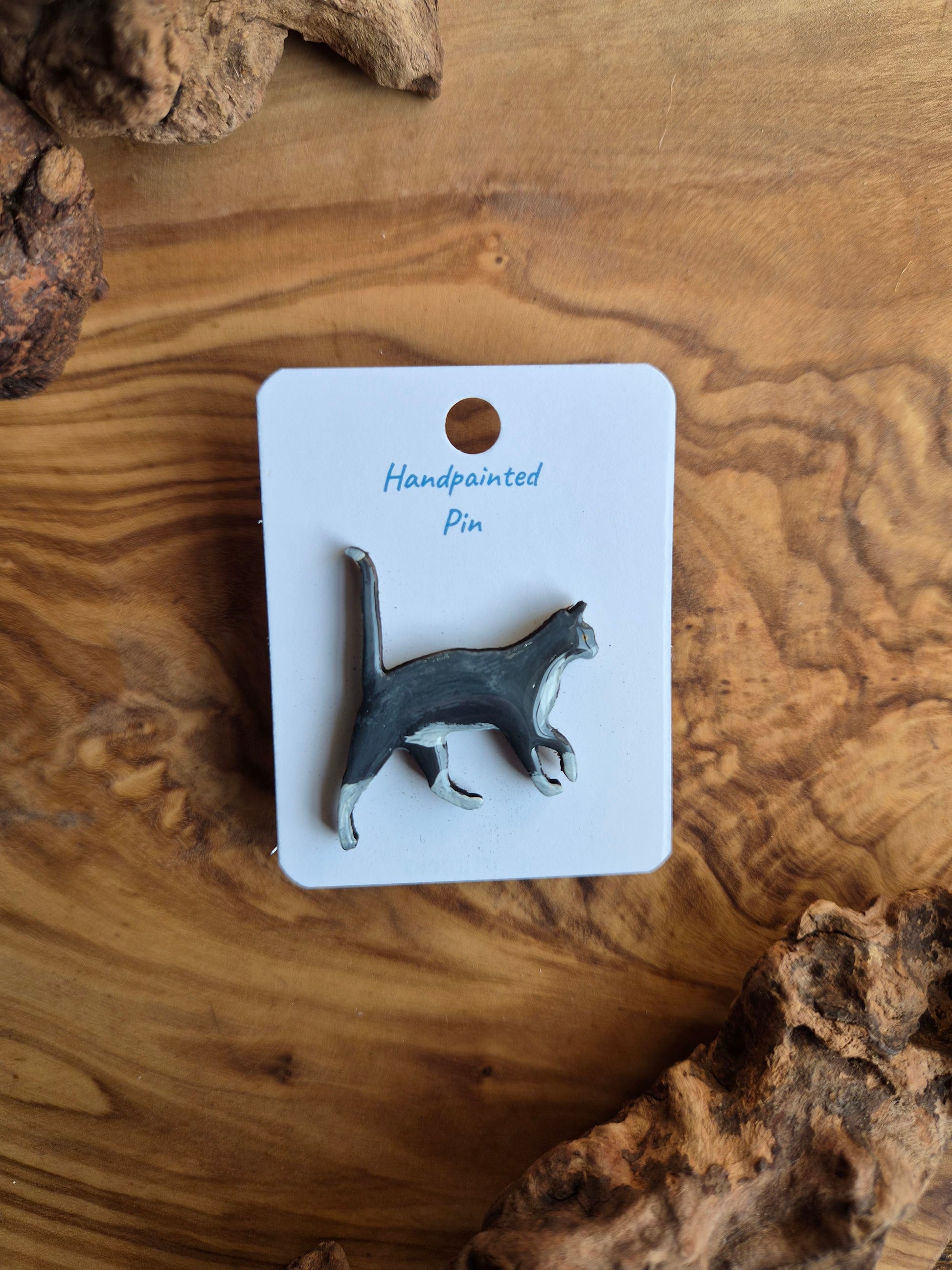 Hand-painted wooden pin badge of a grey cat with white paws and belly
