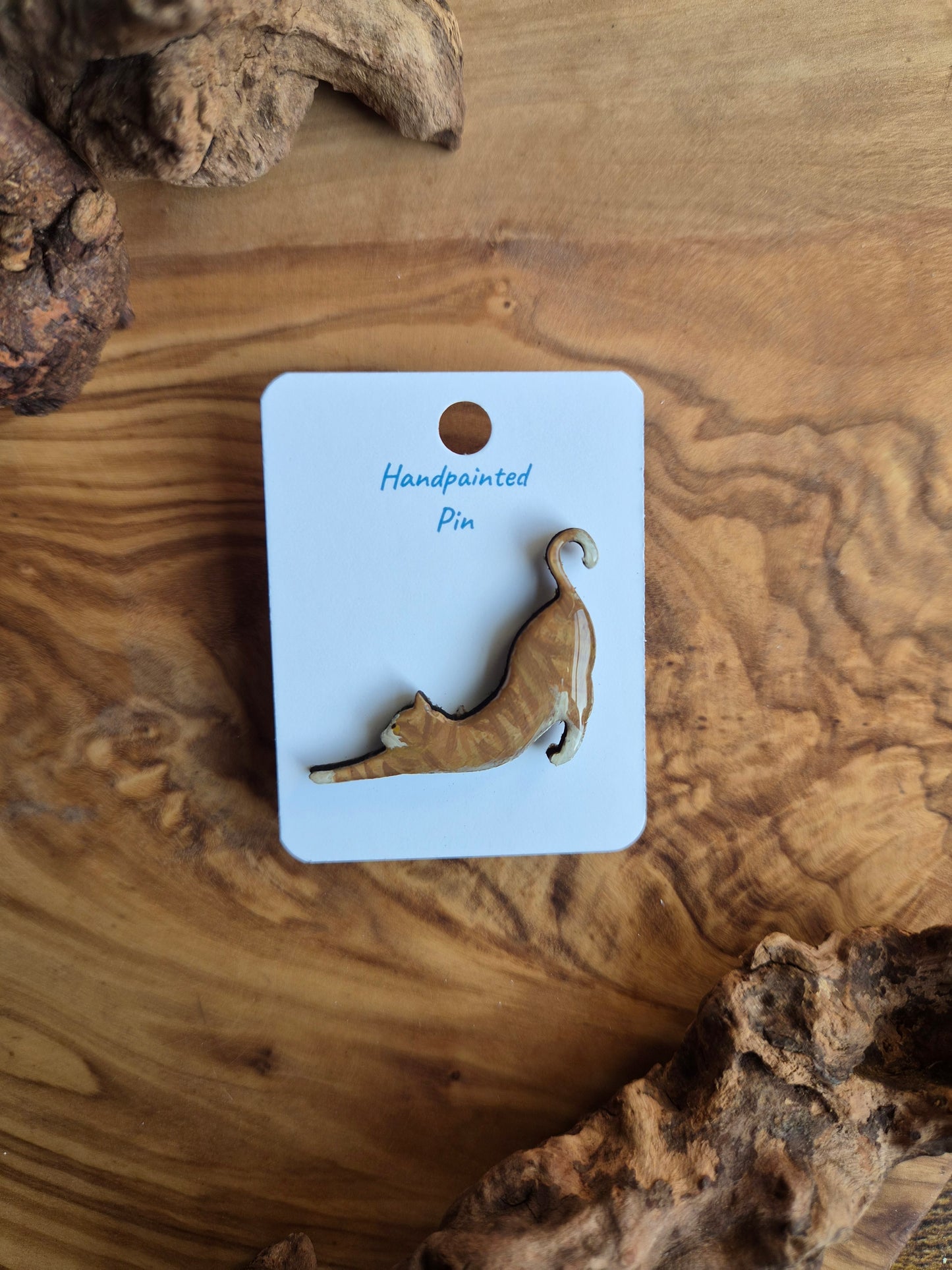 Hand-painted wooden pin badge of a ginger coloured cat with white in a stretching pose
