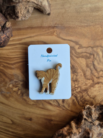 Hand-painted wooden pin badge of a ginger coloured cat with white in an arch pose stretching