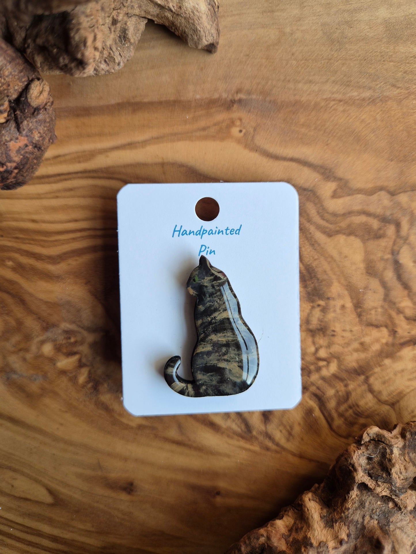 Hand-painted wooden pin badge of a tortoiseshell coloured cat sitting