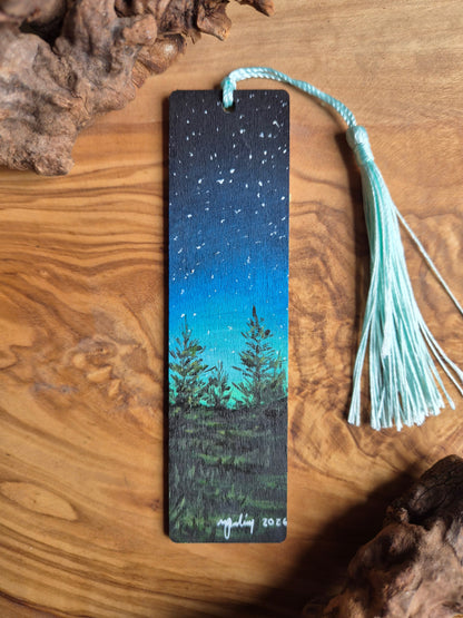 Hand-painted wooden bookmark of glowing aurora borealis behind a tree line silhouette