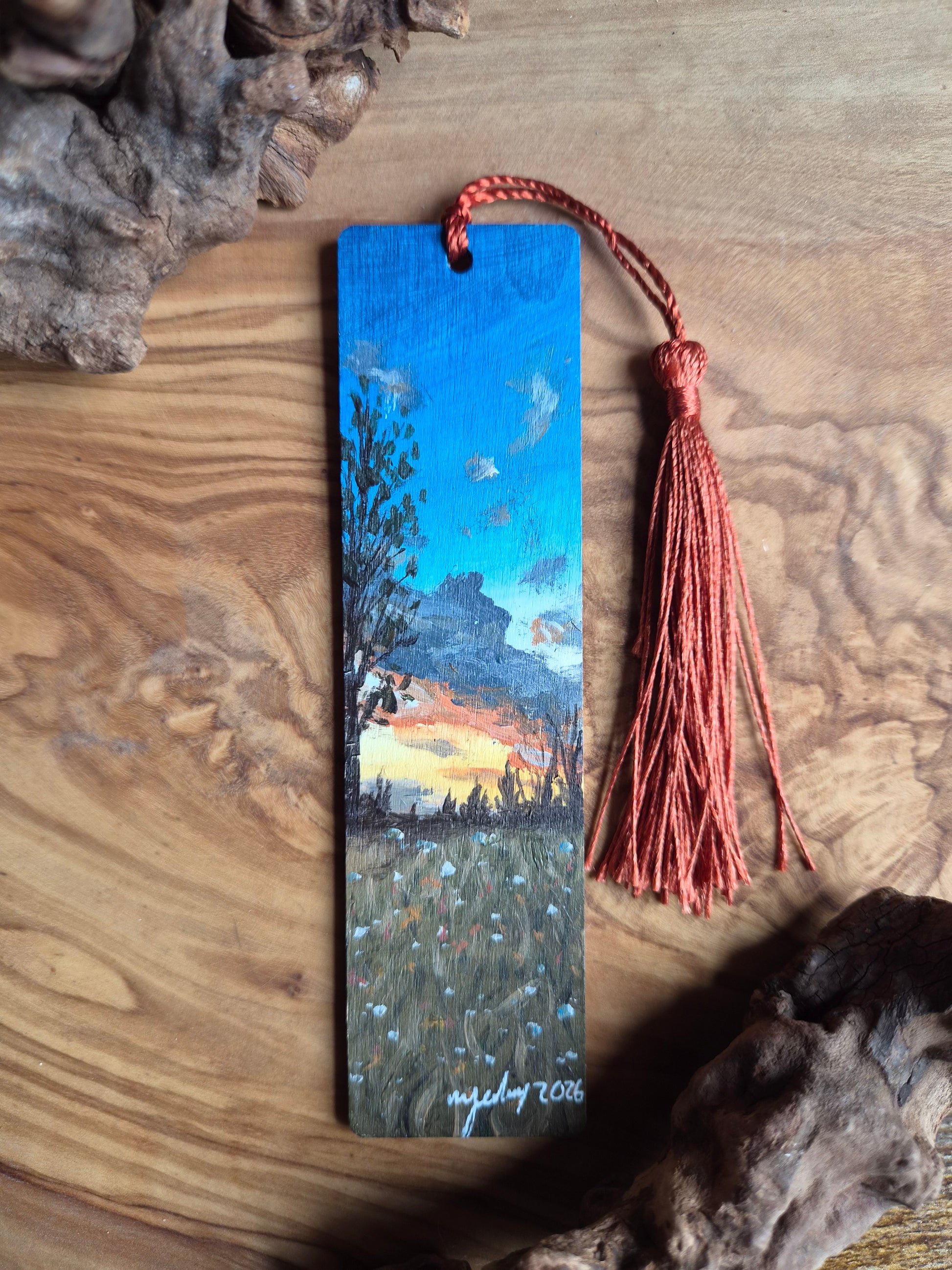 Bookmark with a scenic sunset painting on a wooden surface