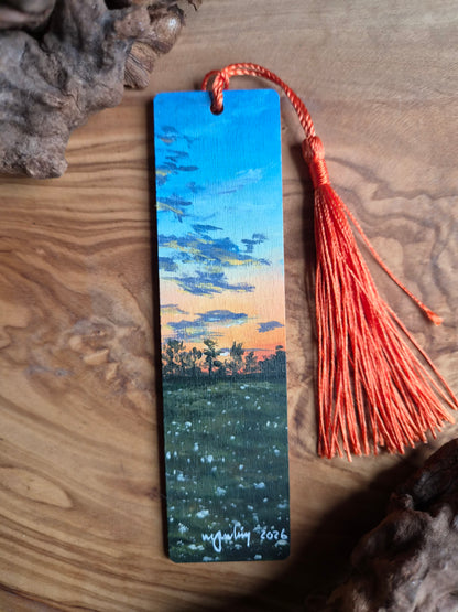 Hand-painted wooden bookmark of a vibrant organge glowing sunset in a field with a treeline 