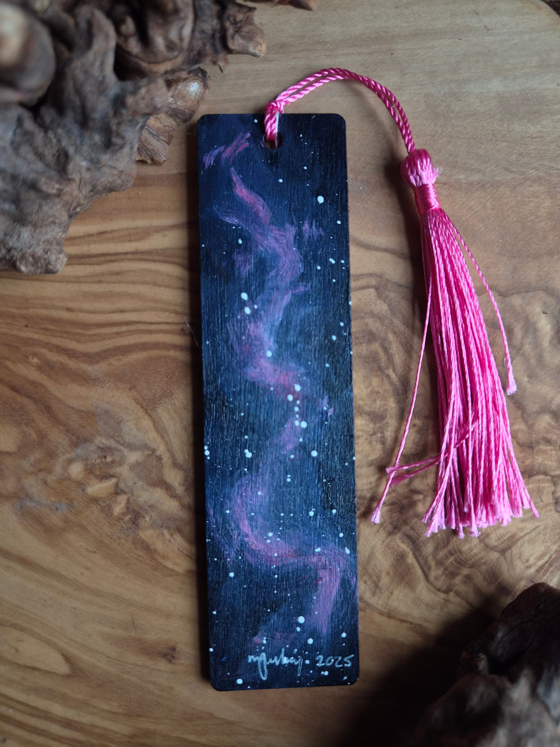 Hand-painted nookmark with galaxy design and pink tassel on a wooden surface
