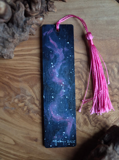 Hand-painted nookmark with galaxy design and pink tassel on a wooden surface