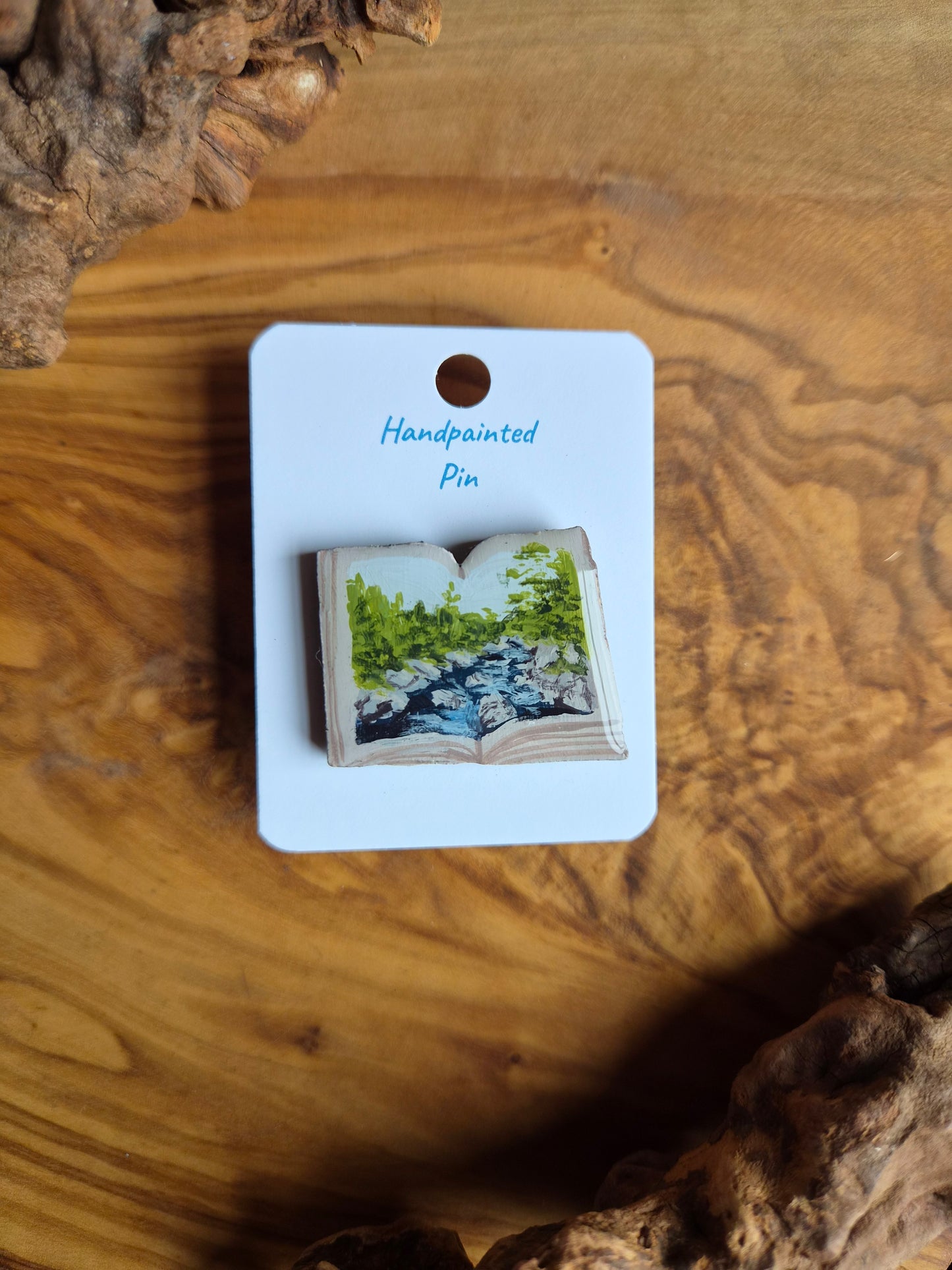 Hand-painted pin badge of an open book shape with a view of the River Findhorn at Randolph's Leap near Logie painted inside, painted onto wood