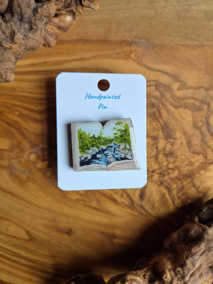 Hand-painted pin badge of an open book shape with a view of the River Findhorn at Randolph's Leap near Logie painted inside, painted onto wood