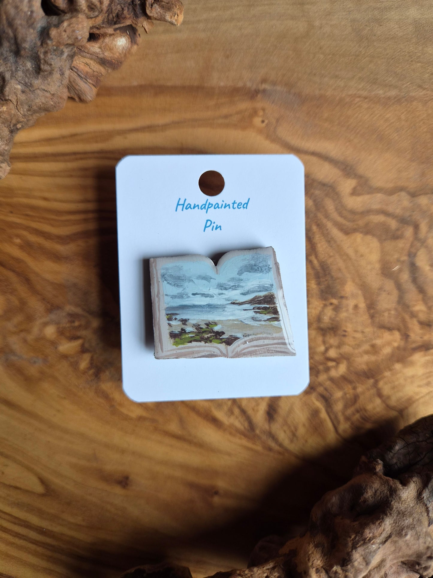 Hand-painted pin badge of an open book shape with a view of Hopeman Beach painted inside, painted onto wood