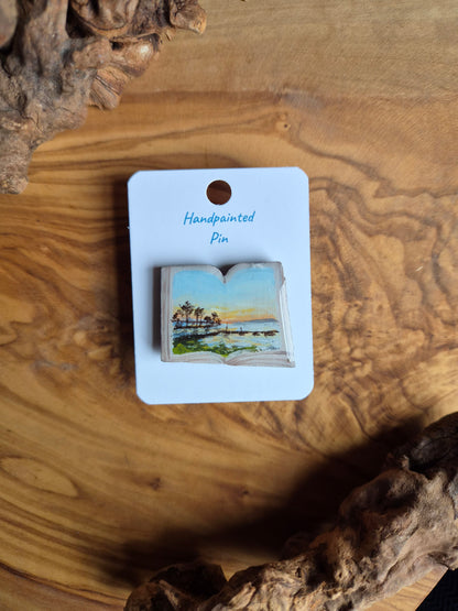 Hand-painted pin badge of an open book shape with a view of a sunrise over Lake Dora in Mount Dora, Florida painted inside, painted onto wood